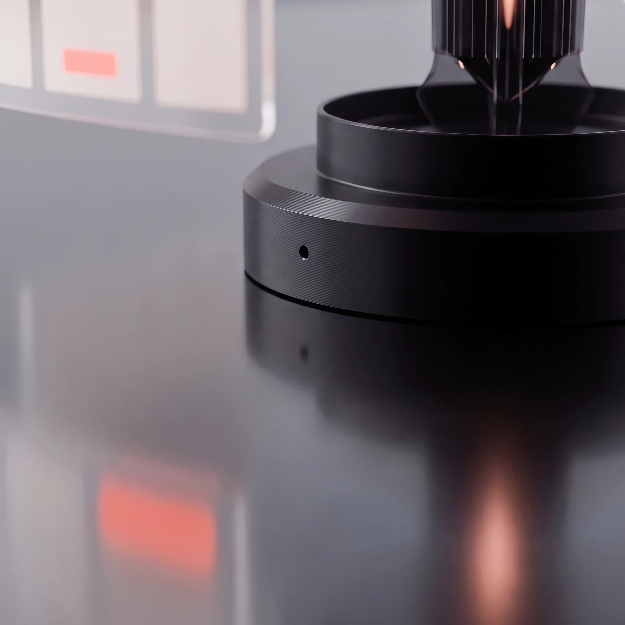Close view of the plinth's machined lower rim and the crisp line where the black metal meets its own reflection, one page panel and its coral accent blurred at the edge of frame and glowing again in the mirror surface below